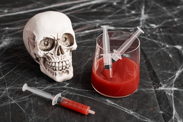 Skull Next to Glass with Syringe and Red Drink on Table